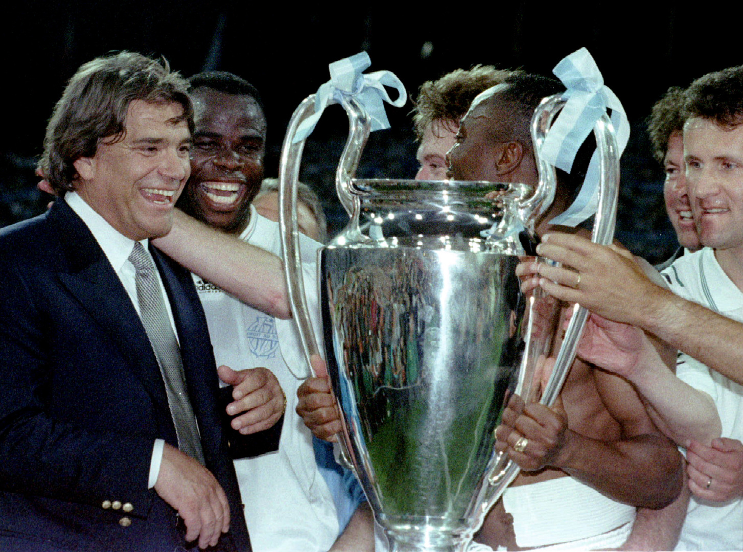 a group of men holding a trophy with one wearing an adidas shirt