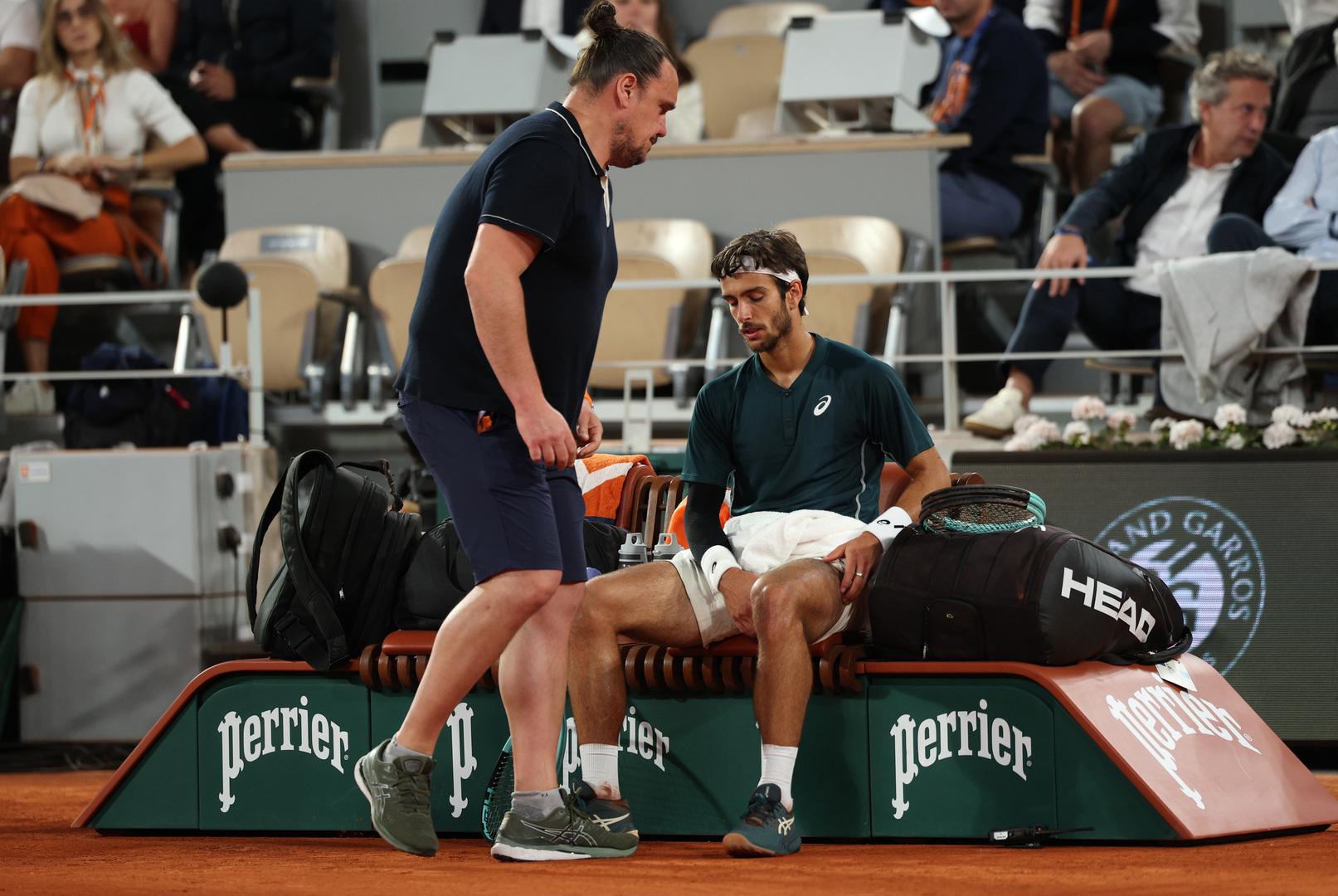Lorenzo Musetti receiving medical attention for his leg during a French Open tennis match.
