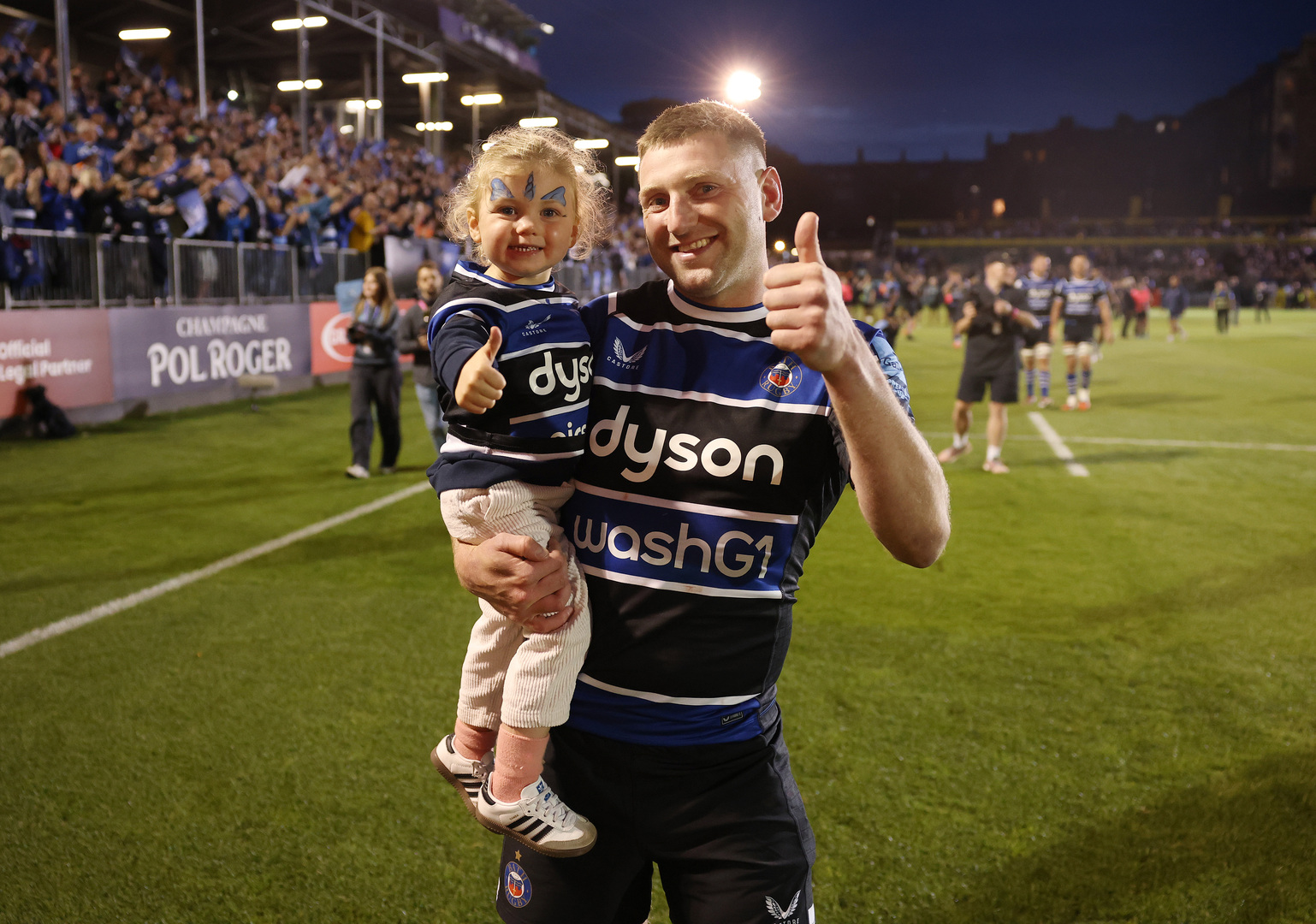 Finn Russell of Bath Rugby holding his daughter after a rugby match victory.