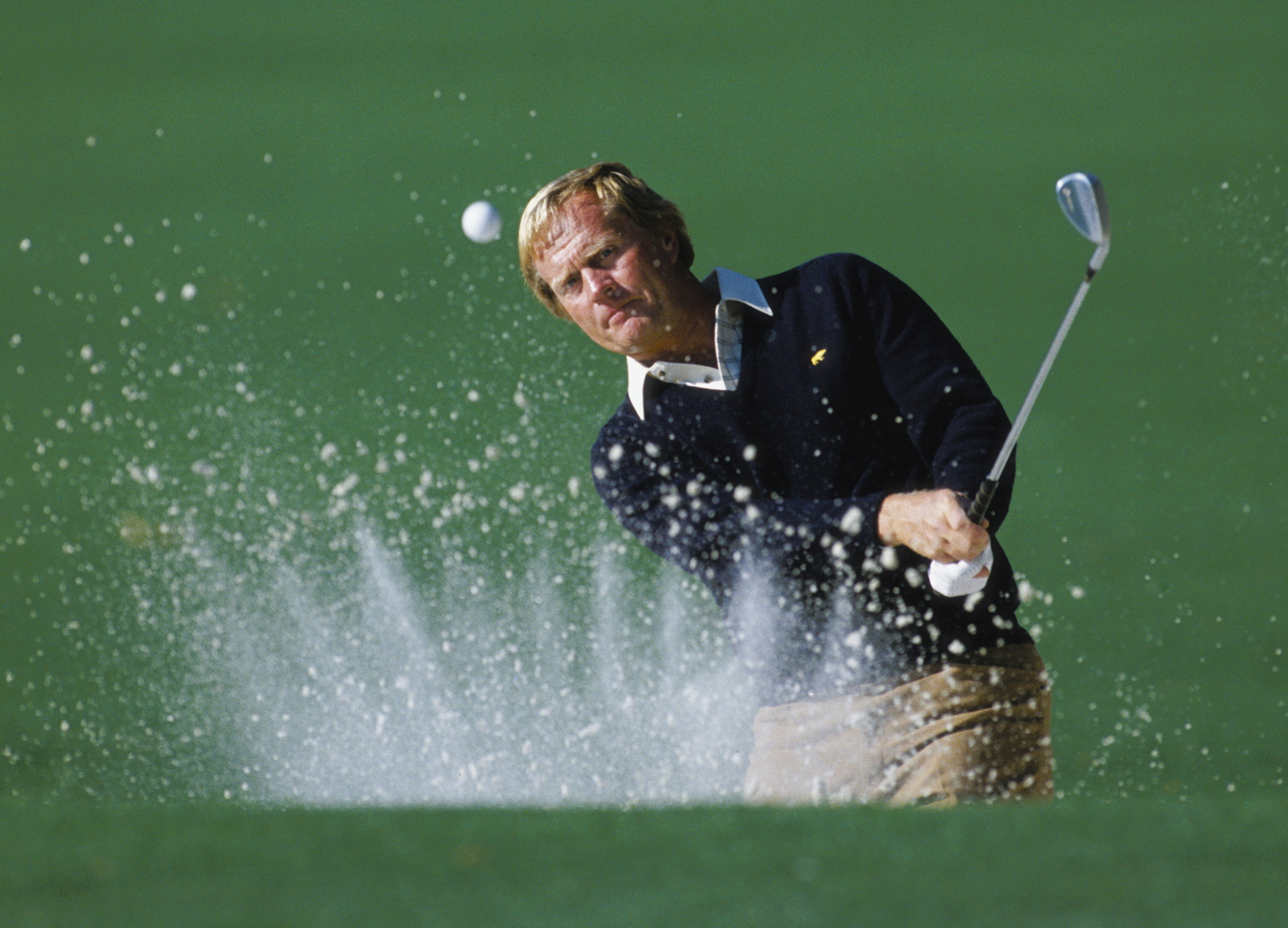Jack Nicklaus hitting a golf ball out of a bunker at the US Masters Tournament.