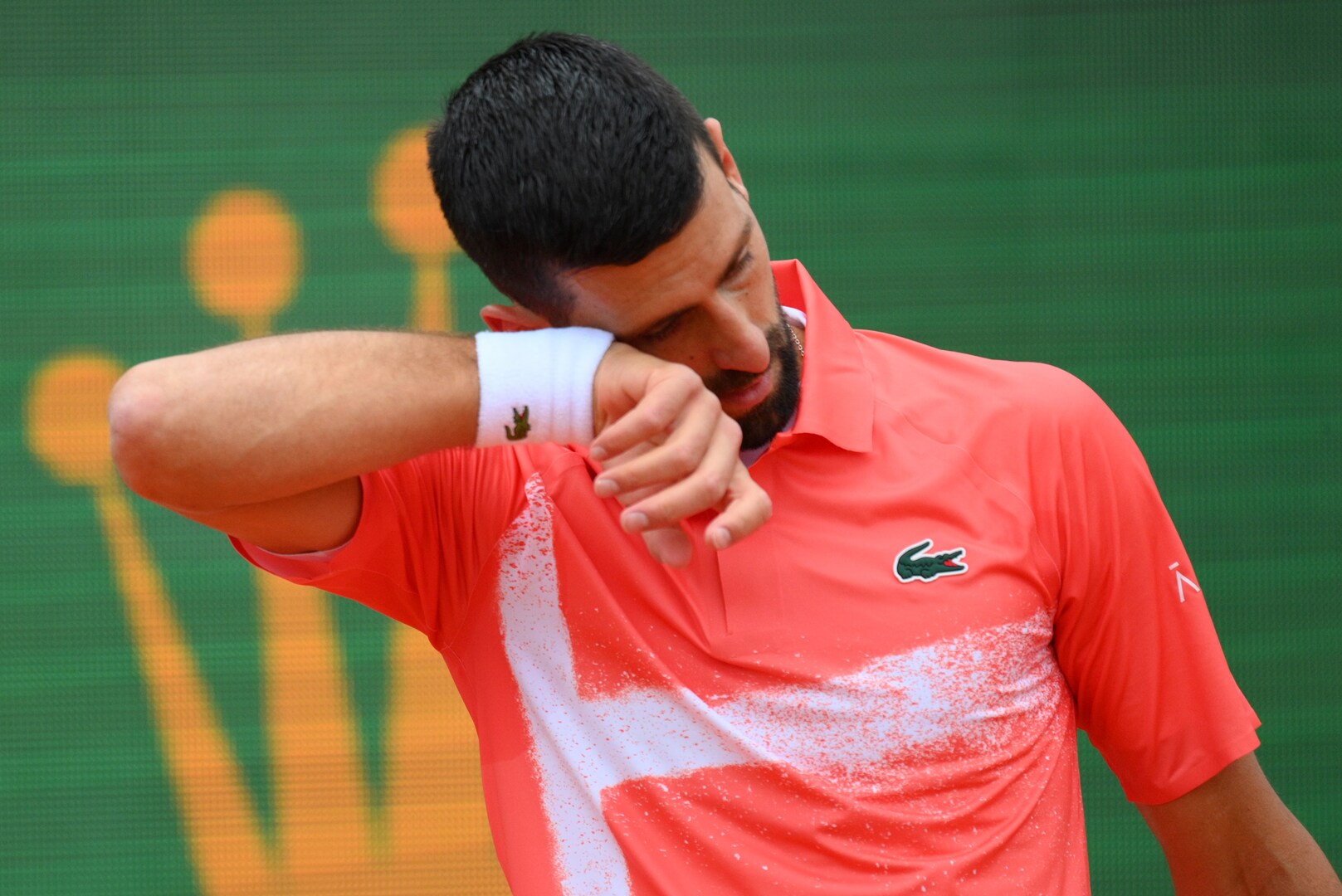 Novak Djokovic wiping sweat from his face during a tennis match.